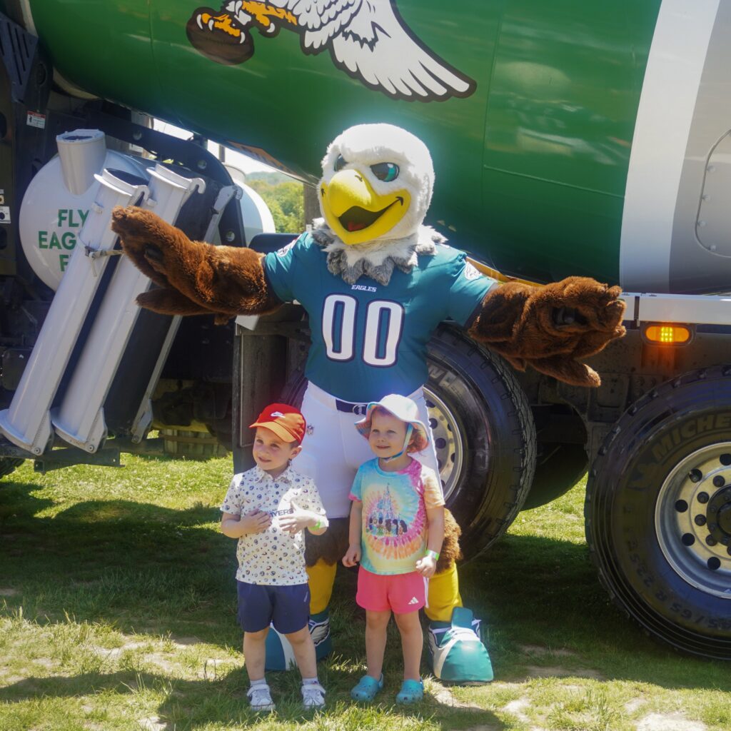 A photo of Philadelphia Eagles' mascot Swoop posing for pictures with attendees in front of a concrete mixer at the Silvi Foundation Touch-a-Truck.